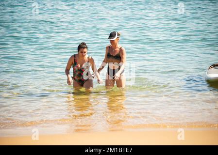 Mother and daughter, in bikinis, are coming out of the water at Porto da Barra beach in Salvador, Bahia. Stock Photo