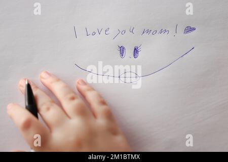 Mothers day. I love you mom inscription on a white sheet and a childs hand with a pen.Holiday of all mothers Stock Photo