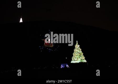 Santa Claus in his sleigh flying overhead with an illuminated Christmas Tree Stock Photo