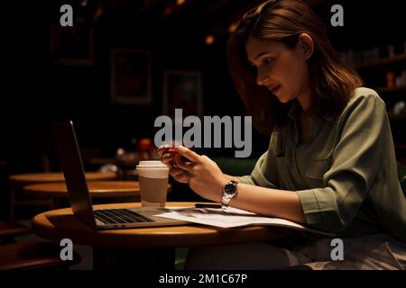 Young woman using smart phone and laptop at cafe. Stock Photo