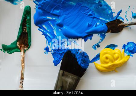 Overhead shot of brushes for painting, puddle of blue, and yellow paint, acrylic paint on light Board. Art concept. Fine art school Stock Photo