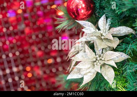 Christmas ornaments and flowers on tree. Red bokeh background. Stock Photo