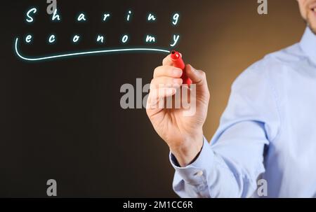 Businessman writing on virtual screen against dark background. Concept of sharing economy Stock Photo