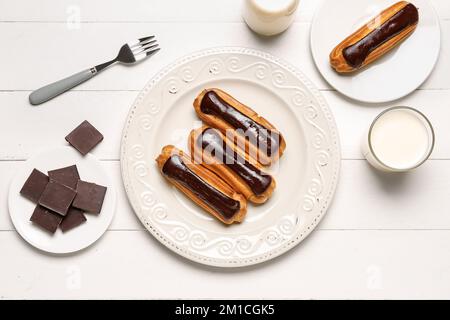 Composition with plates of tasty eclairs, chocolate and milk on light wooden background Stock Photo