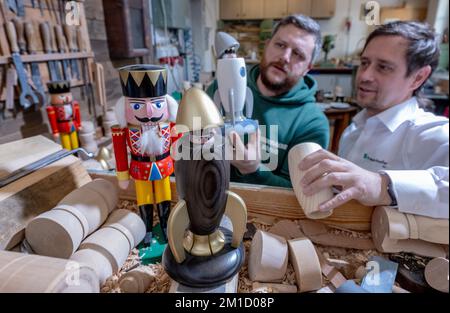 PRODUCTION - 08 December 2022, Saxony, Seiffen: Wooden toy maker Markus Füchtner (l) presents a new smoking rocket in his workshop in Seiffen together with Holger Kunze from the Fraunhofer IWU, which incorporates high-tech material from space travel. Scientists from the Fraunhofer Institute for Machine Tools and Forming Technology spent six months tinkering with the team led by wooden toy maker Markus Füchtner. Now, during Advent, they are raising the curtain on the prototype of their smoking rocket. The warmth of an incense candle opens the tip of the rocket as if by magic and a mini nutcrack Stock Photo