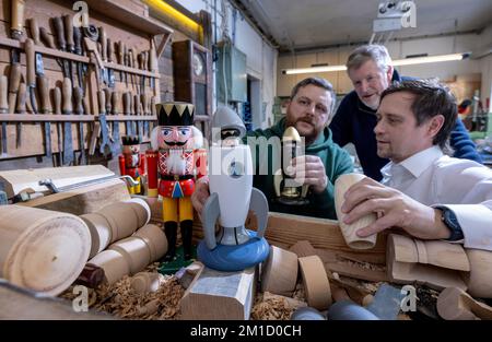 PRODUCTION - 08 December 2022, Saxony, Seiffen: Wooden toy maker Markus Füchtner (l-r) presents a new smoking rocket in his workshop in Seiffen together with partners Wolfgang Braun from the 'Denkstatt Erzgebirge' and Holger Kunze from the Fraunhofer IWU, which incorporates high-tech material from space travel. Scientists from the Fraunhofer Institute for Machine Tools and Forming Technology worked for six months with the team led by wooden toy maker Markus Füchtner. Now, during Advent, they are raising the curtain on the prototype of their smoking rocket. The warmth of an incense candle opens Stock Photo