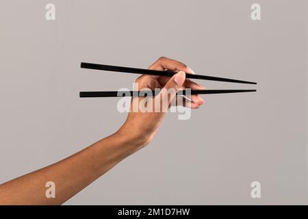Crop anonymous African American female showing black chopsticks against gray background in studio Stock Photo