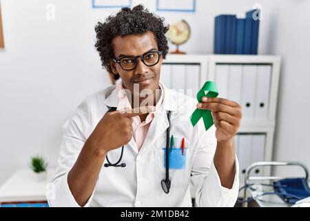 African doctor man holding support green ribbon smiling happy pointing with hand and finger Stock Photo
