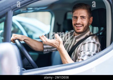 Hispanic man with beard driving car celebrating achievement with happy smile and winner expression with raised hand Stock Photo