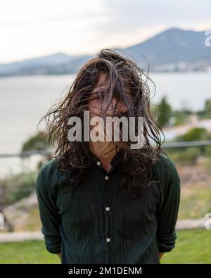 A portrait of a young man with long curly hair posing in a park during the wind Stock Photo