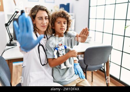 Young kid at pediatrician clinic holding teddy bear with open hand doing stop sign with serious and confident expression, defense gesture Stock Photo
