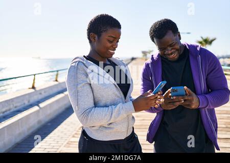 Man and woman couple wearing sportswear using smartphone at seaside Stock Photo