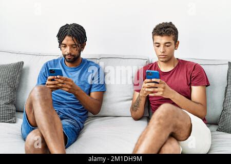Two men friends using smartphone sitting on sofa at home Stock Photo
