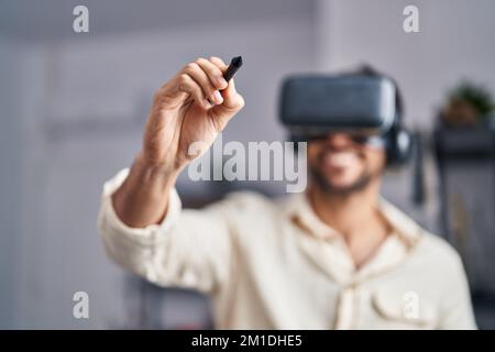 Young hispanic man artist using virtual reality glasses drawing at art studio Stock Photo