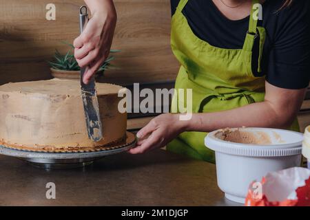 Unrecognisable woman decorating a delicious layered sponge cake with chocolate icing cream. DIY, sequence, step by step, part of series. Stock Photo