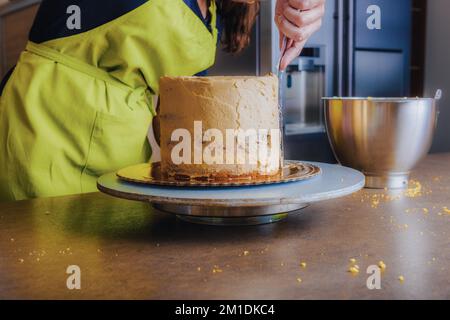 Unrecognisable woman decorating a delicious layered sponge cake with chocolate icing cream. DIY, sequence, step by step, part of series. Stock Photo