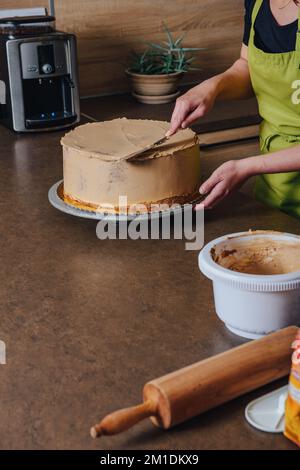 Unrecognisable woman decorating a delicious layered sponge cake with chocolate icing cream. DIY, sequence, step by step, part of series. Stock Photo