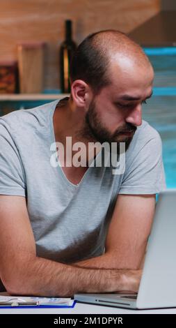 Entrepreneur sitting in remotely office working on laptop computer holding head with hands looking down. Busy focused employee using modern technology network wireless doing overtime for job reading Stock Photo