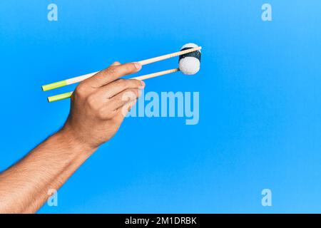 Hand of man holding sushi with chopsticks over isolated blue background Stock Photo