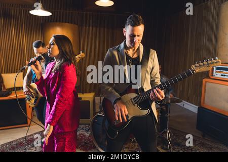 Musicians in recording studio. Process of creating a music album. Group members - mid adult male guitarist and fashionable female singer - in the foreground. High quality photo Stock Photo