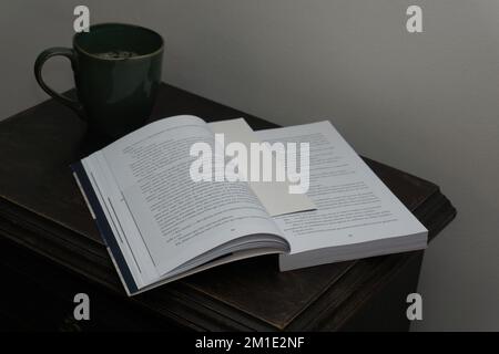 Open book and coffee cup on bedside table Stock Photo