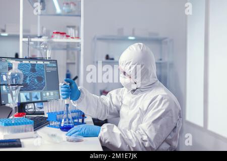 Medical researcher measuring liquid using automatic pipette in micriobiology lab. Chemist in modern laboratory doing research using dispenser during global epidemic with covid-19. Stock Photo
