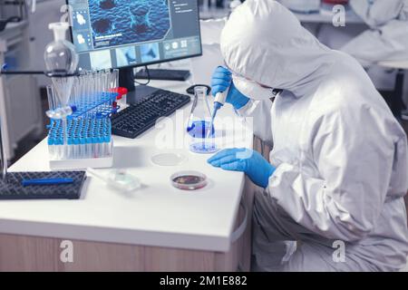 Focused lab technician pipetting solution into petri dish working on his workplace in modern lab. Chemist in modern laboratory doing research using dispenser during global epidemic with covid-19. Stock Photo