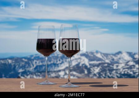 Two glasses of red wine against mountain background. View of snowy peaks in the mountains. Stock Photo