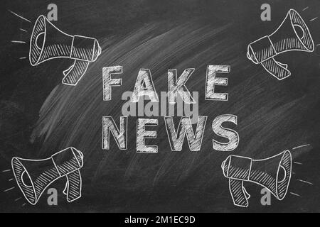 Megaphones with the text FAKE NEWS drawn in chalk on a blackboard. Hand drawn illustration. Information and disinformation concept. Stock Photo