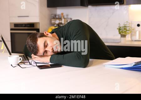 Man falling sleep while working remotely from his kitchen Stock Photo