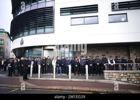 Police and members of the public 'observe a silence' outside St Helier Police Station, following an explosion and fire at a block of flats in St Helier, Jersey. Police have said that five people are now confirmed to have died following the blast. Picture date: Monday December 12, 2022. Stock Photo