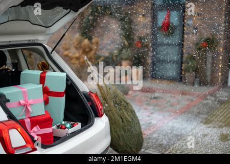 Gift boxes in vehicle trunk in front of a house decorated for winter holidays Stock Photo