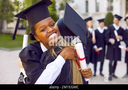Two happy female students hugging during graduation ceremony at college or university. Stock Photo