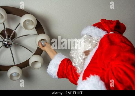 Santa changes the burned-out light bulbs in the chandelier Stock Photo
