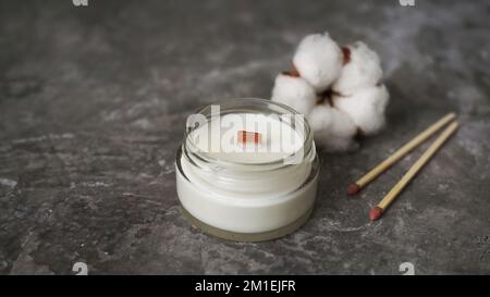 Label mockup of the glass jar with handmade candle with a wooden wick, long matches, cotton flower. Cozy home interior on a marble background Stock Photo