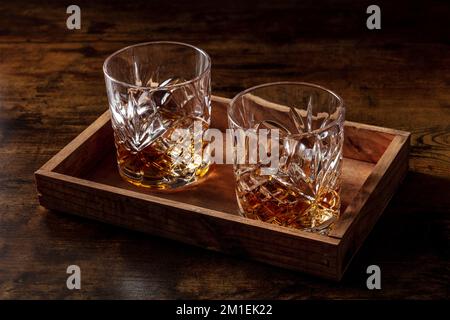 Whiskey in glasses with ice. Bourbon whisky on rocks on a dark rustic background, elegant drinks, moody shot Stock Photo