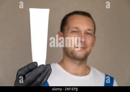Employee in blue uniform and white T-shirt holds white tube on which you can place logo or text. Space for copying. Stock Photo