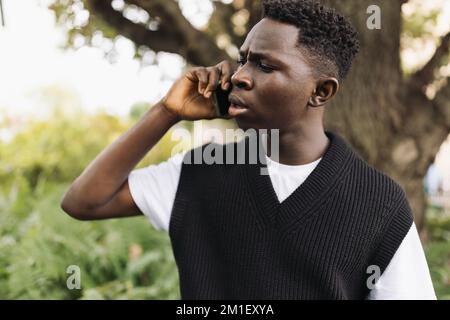 Young African man talking on phone shocked, stressed. Street portrait, copy space Stock Photo