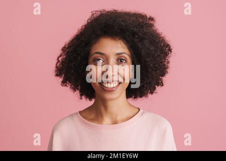 Black happy woman with afro hairstyle smiling and looking at camera isolated over pink background Stock Photo