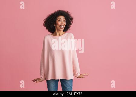 Black happy woman with afro hairstyle smiling and looking at copyspace isolated over pink background Stock Photo