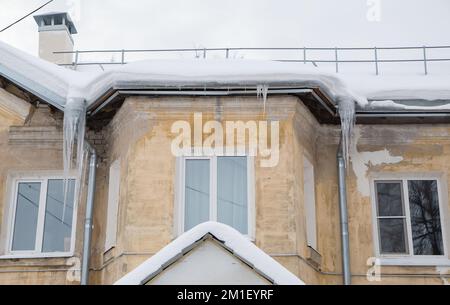 Long, frozen icicles hang on a drainpipe, spring or winter. Wall of an old brick house with windows. Large cascades of icicles in smooth, beautiful rows. Cloudy winter day, soft light. Stock Photo