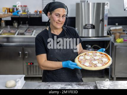Female chef with pizza in restaurant kitchen Stock Photo