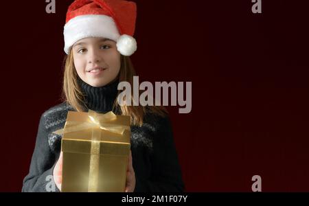 Christmas vertical banner with a teenage girl in a Santa hat and a gift box. dark red burgundy background. place for text Stock Photo