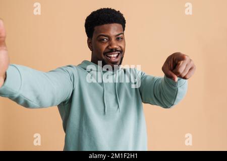 Black bearded young man smiling and taking selfie photo isolated over beige background Stock Photo