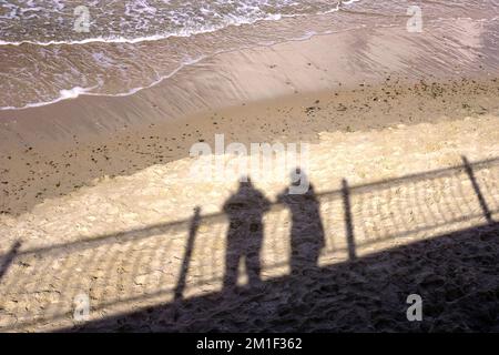 Shadow on the beach sand of two loving people, standing near parapet seeing on sea waves on sand beach Stock Photo