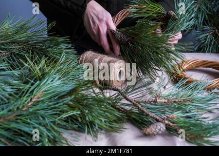 Making rustic Christmas wreath. Female hands on background of  wooden table with pine tree branches, cones, lights.Holiday preparations Stock Photo