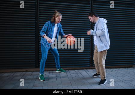 Man with down syndrome playing basketball outdoor with his friend. Concept of friendship and integration people with disability into society. Stock Photo