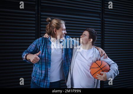 Man with down syndrome playing basketball outdoor with his friend. Concept of friendship and integration people with disability into society. Stock Photo