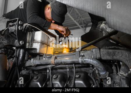 Car mechanic repairs large truck or tractor in workshop. Professional mechanic repairs truck engine. Genuine worker.. Stock Photo