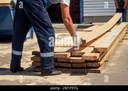 Workers wear wooden planks on sawmill or in carpentry shop. Authentic workflow. Timber harvesting for construction. Carpenters stack boards. Industrial background.. Stock Photo
